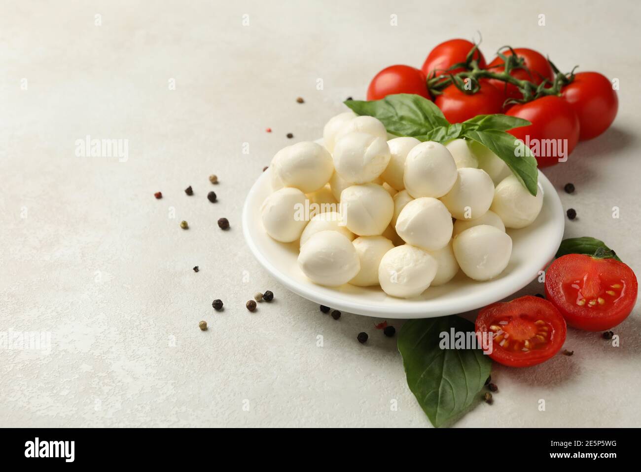 Plate with mozzarella and basil, tomato and pepper on white textured background, space for text Stock Photo