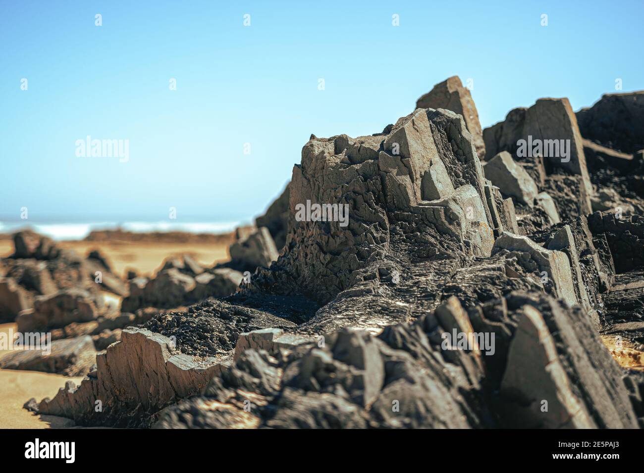 Black rock volcanic formation on sand beach. Square stones on the coast. Portugal, Algarve coastline. Stock Photo