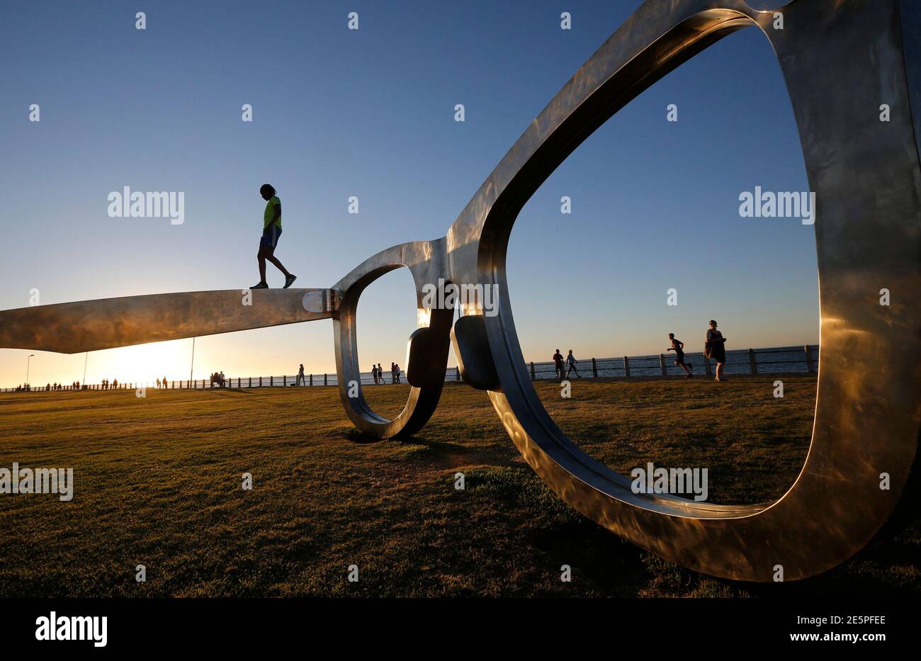 A youth climbs on top of a sculpture in the form of a giant pair of spectacles on Cape Town's Sea Point Promenade, November 18, 2014.  Inspired by Nelson Mandela, the work  'Perceiving Freedom' by artist Michael Elion has stirred some controversy in the local media. While popular with visitors to the promenade, some critics have questioned the association of Mandela's legacy with commercial sponsors.  REUTERS/Mike Hutchings (SOUTH AFRICA - Tags: SOCIETY) Stock Photo