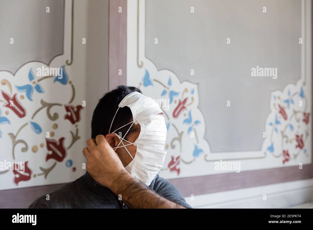 Interior shot  profile portrait of an unrecognizable man with multiple protective masks and his hand adjusting the straps on ear. Stock Photo