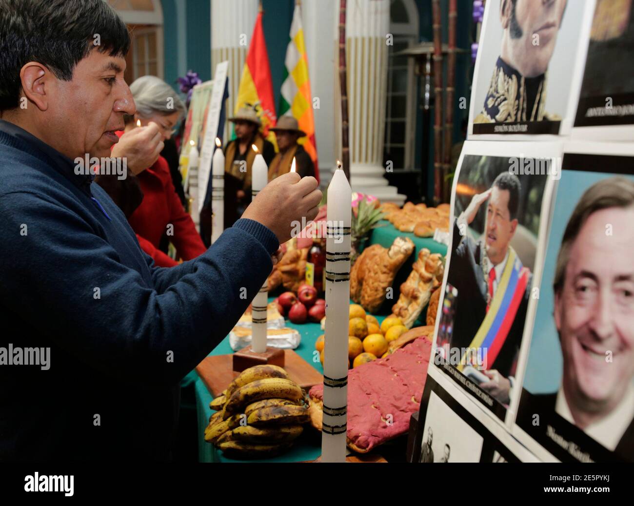 Bolivian Foreign Minister David Choquehuanca lights a candle during an All Saints' Day celebration in front of images depicting Argentine former president Nestor Kirchner and Venezuela's Hugo Chavez in La Paz, November 1, 2013. Traditionally, indigenous Bolivians celebrate All Saints Day by paying homage to their dead ones with a feast of home-baked, doll-shaped breads, fresh fruit and coca leaves and flowers. The syncretism practiced by the Aymaras, a blend of Catholicism and indigenous beliefs, calls for the offerings to be neatly placed on top of graves, and then to give them away to beggar Stock Photo
