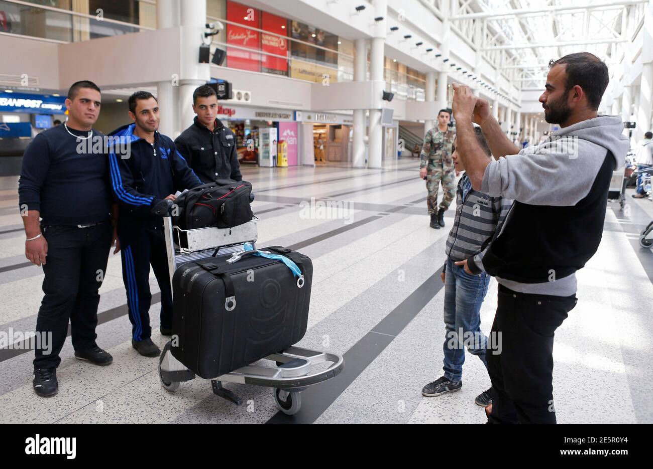 A man takes a photograph of a man (2nd L), who said he is leaving Lebanon for good for Australia, at Beirut's international airport, March 28, 2014.  In both war and peace, Lebanon has always seen many of its ambitious youth leave for better opportunities. More Lebanese live outside Lebanon than in it. But neighbouring Syria's civil war, bombs in Lebanon and an economic slowdown have eroded confidence in the country's future and now even loyal patriots are scrambling to get out. To match story SYRIA-CRISIS/LEBANON-YOUTH    REUTERS/Mohamed Azakir (LEBANON - Tags: POLITICS TRANSPORT SOCIETY IMMI Stock Photo