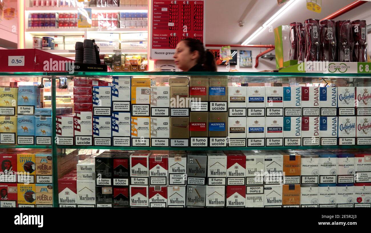 An employee walks past cigarette packets next to an information board which displays the price of cigarettes when purchased in Italy (L) and France (C) with the difference in savings (R), in a supermarket in Latte, near the Franco-Italian border, January 13, 2014. The prices of cigarettes have increased in France on January 13, 2014. REUTERS/Eric Gaillard   (ITALY- Tags: BUSINESS Stock Photo