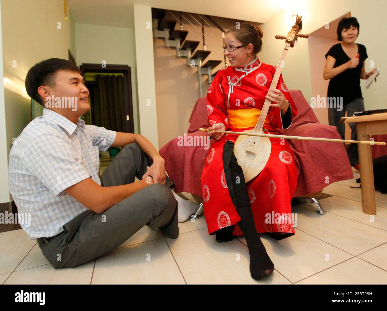 Australian citizen Elizabeth Gordon (C), dressed in a Tuvan national costume, plays the Tuvan ethnic musical instrument called Igil inside the house of local Saryglar family, where Elizabeth lives, in the Kyzyl town, the administrative centre of Russia's Tuva region, some 800 km (497 miles) south of the Siberian city of Krasnoyarsk, September 12, 2011. Elizabeth from the state of Queensland, Australia, arrived in the Siberian region of Tuva in April, 2010 to study the Russian and Tuvan languages, the culture, traditions and music of the Tuvans, one of the native peoples of Siberia. The enthusi Stock Photo