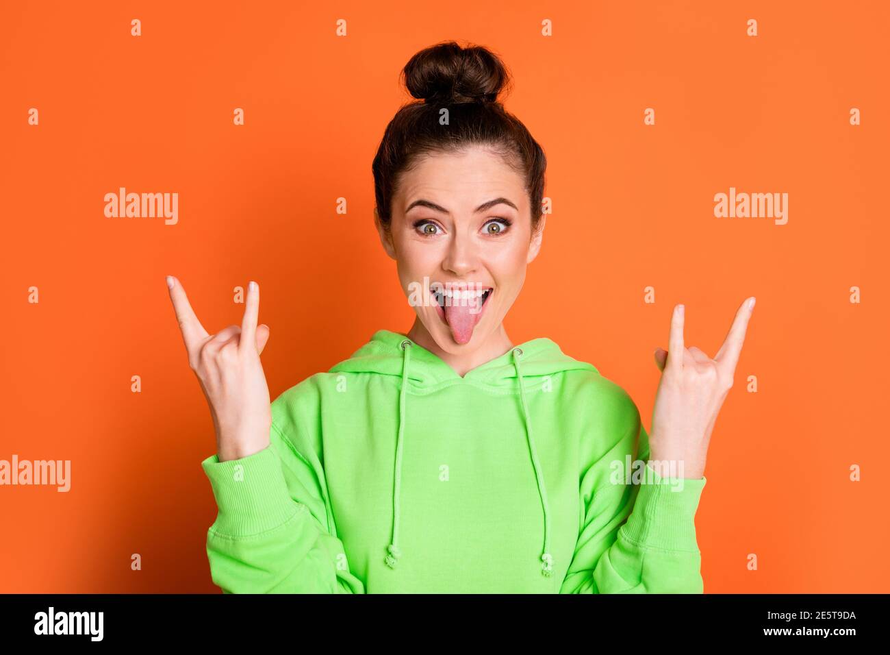 Photo of lovely tricky young lady dressed green sweatshirt showing heavy rock sign isolated bright orange color background Stock Photo