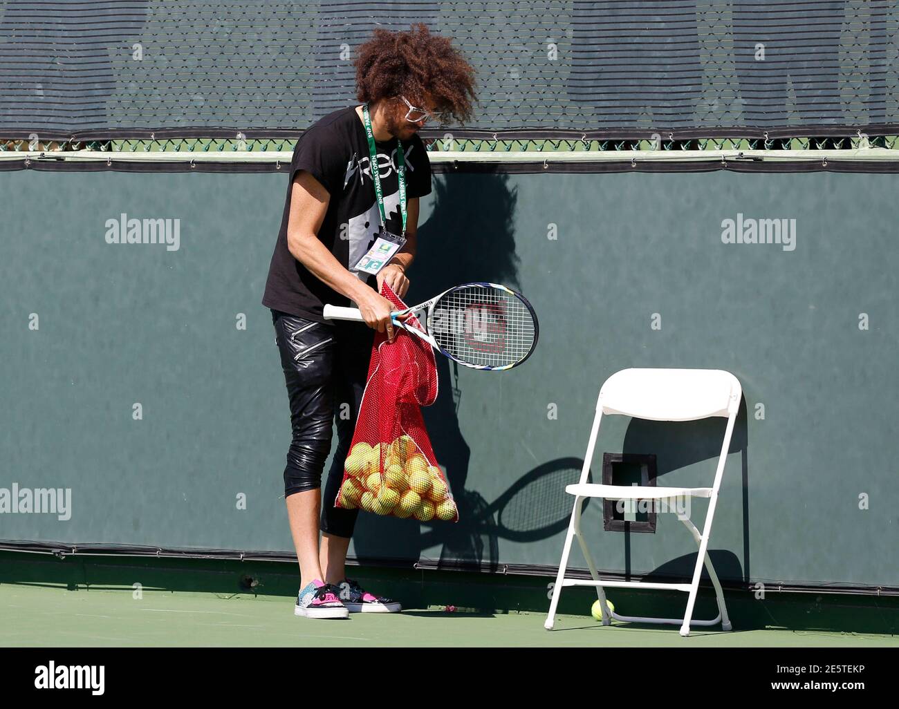 Redfoo, also known as Stefan Gordy of the band LMFAO, collects tennis balls  as his girlfriend Victoria Azarenka of Belarus attends a practice session  to prepare for the BNP Paribas Open WTA
