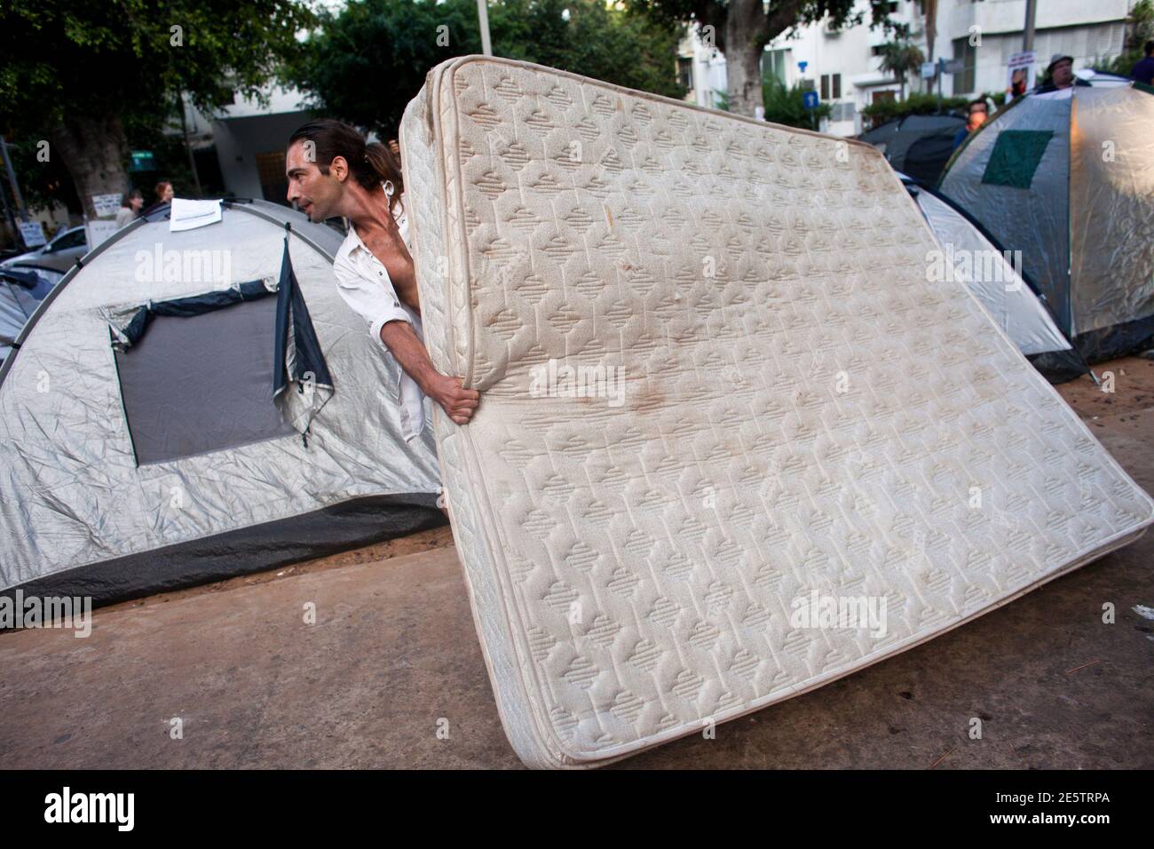An Israeli protester carries a mattress near tents pitched on Tel Aviv's Rothschild Boulevard during a demonstration against high housing prices, July 18, 2011. Similar protests have been planned in other Israeli cities where rental costs have skyrocketed as a result of a shortage in available dwellings in primary locations. REUTERS/Nir Elias (ISRAEL - Tags: POLITICS BUSINESS SOCIETY) Stock Photo