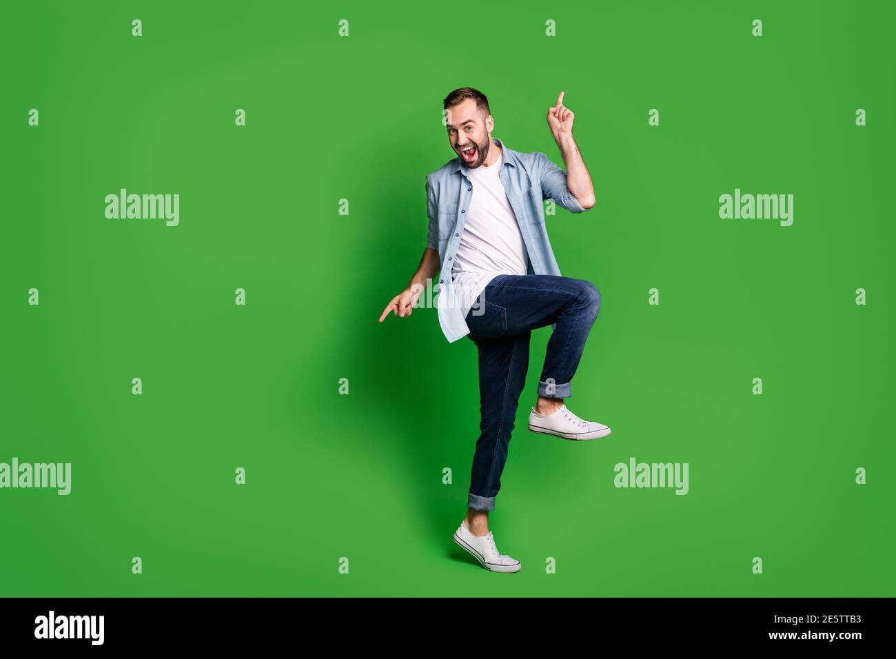 Full size photo of optimistic guy dancing wear blue shirt jeans footwear isolated on green color background Stock Photo