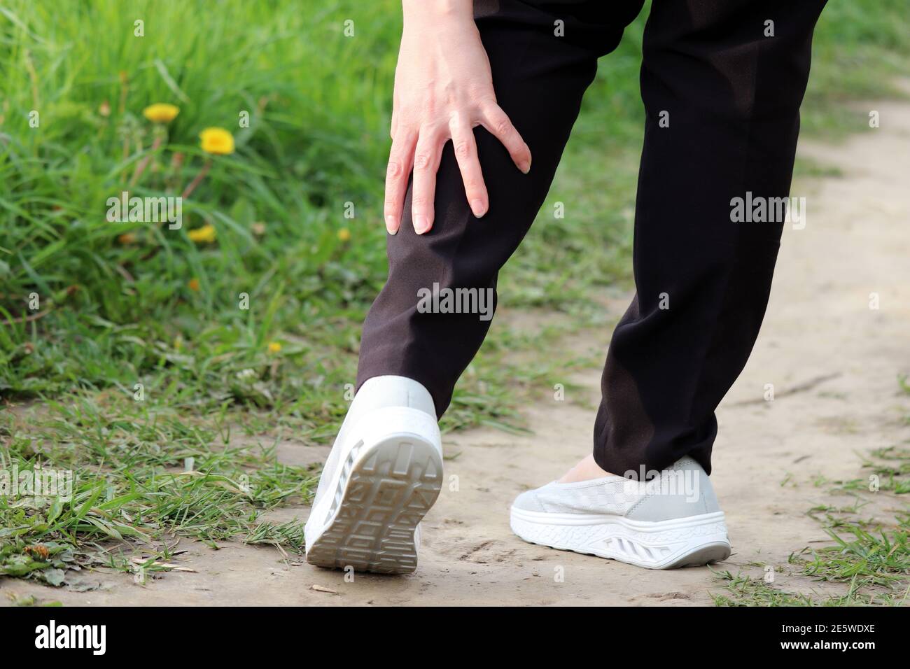 Ankle sprain, woman grabbed her leg while walking on a nature. Concept of tired legs, injury on running Stock Photo