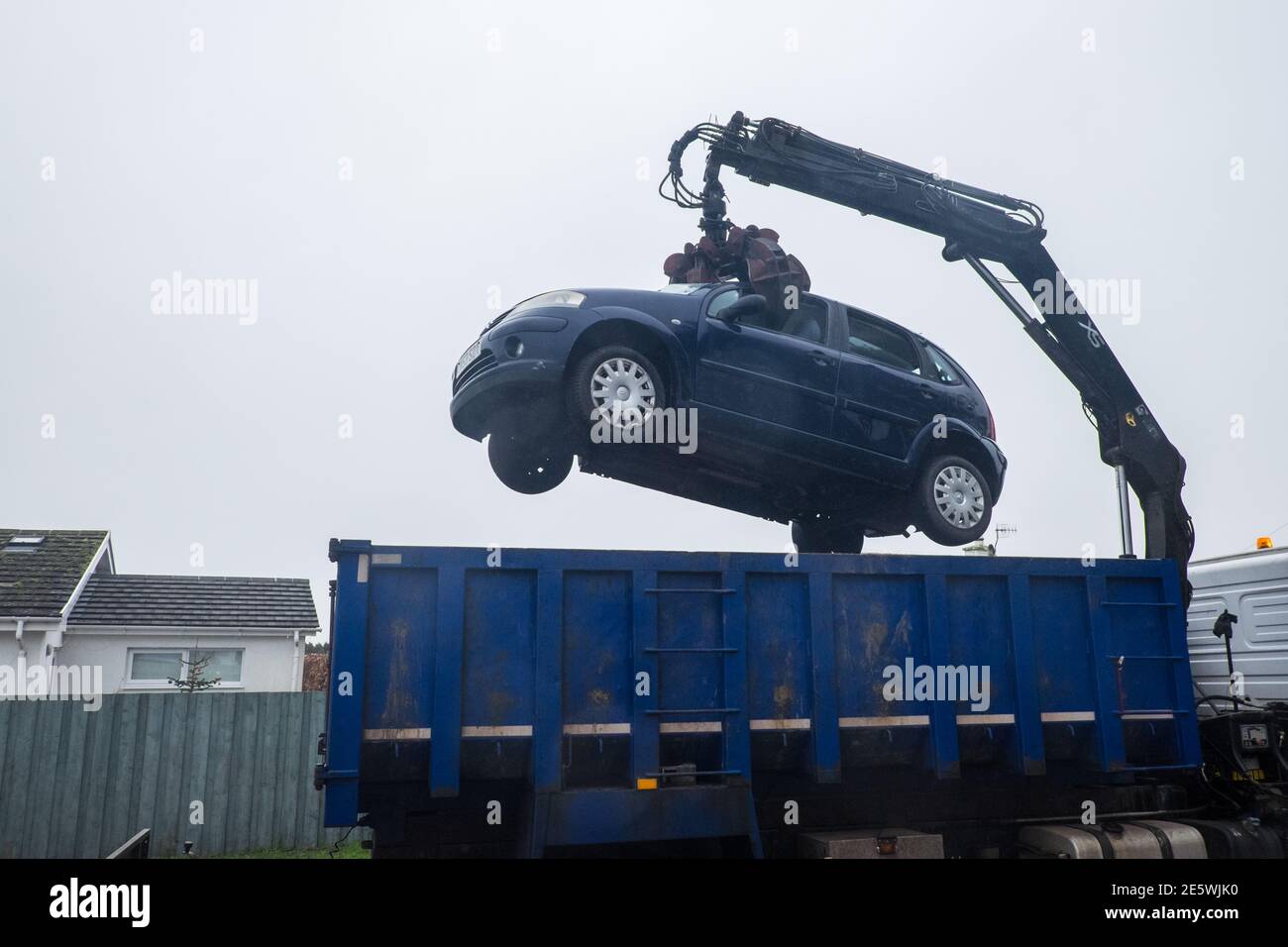 My, private, vehicle,car,a,France,French,made,built, Citroen C3,blue,hatchback,being,removed,by,crane,truck,from,my,driveway,to,be,scrap,scrapped.No,longer,economically,viable,to,maintain,due,to,rust,and,not wanting to throw good money after badge decision, had to be made to destroy vehicle. Failed, MOT. DVLA, Photo taken in seaside resort of Borth,a,few,miles,north,of,Aberystwyth,Ceredigion,Mid,West Wales,Welsh,holiday destination.UK,Europe,mobile,scrapyard,end of life,gone,waste,consumption,throw away,society,recycling,reuse,not,metal,cars,vehicles,crush,grabber,machine,grabbing, Stock Photo