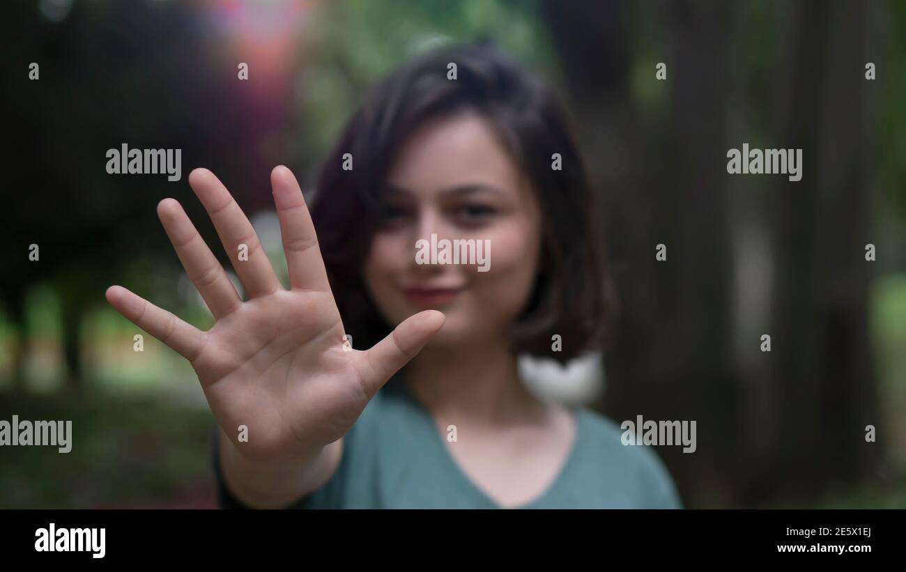 Young woman smiling and strect her hand wide open to forward. Gesture which means stop shown by young beautiful female model.  Focus is on hand. Stock Photo