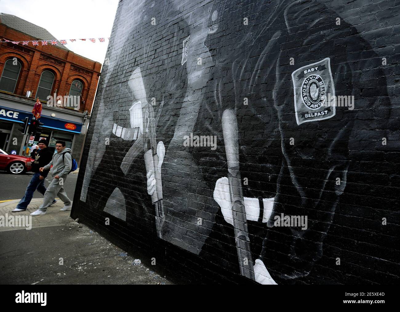 Locals pass a mural showing loyalist Ulster Volunteer Force (UVF) gunmen on a wall in a predominantly protestant area of east Belfast June 23, 2011. The violence in the Catholic Short Strand enclave of mainly Protestant east Belfast has come at the start of the 'marching season', a time of annual parades by Protestants which has triggered violent protests by Catholics in the past.  REUTERS/Dylan Martinez   (NORTHERN IRELAND - Tags: CIVIL UNREST POLITICS IMAGES OF THE DAY) Stock Photo