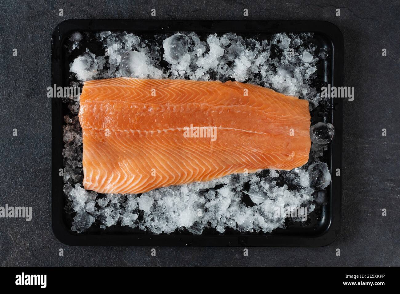 Fresh raw salmon fish fillet on ice on black background top view. Healthy food full of omega 3