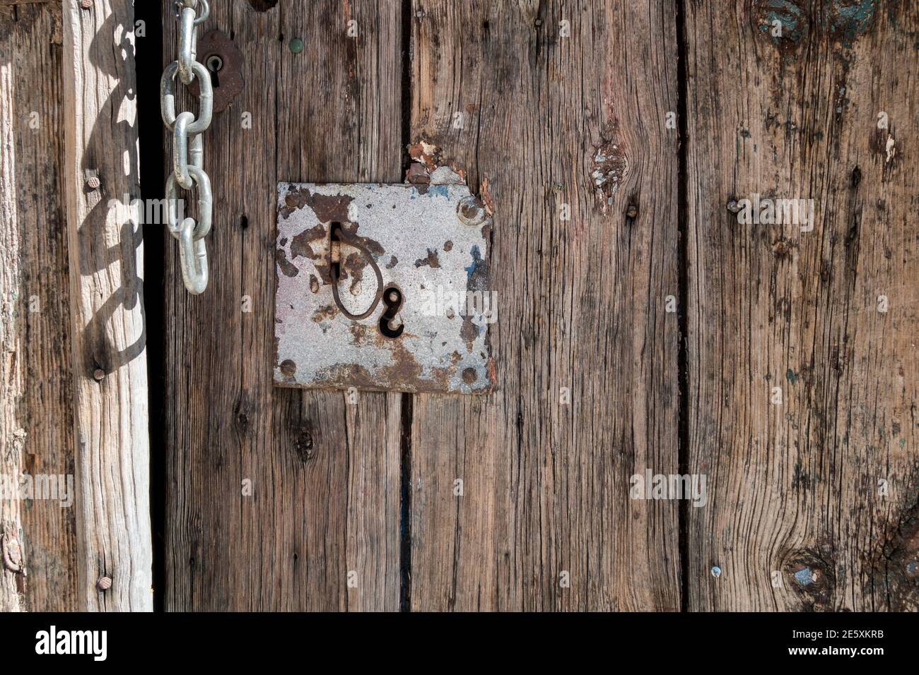 Design detail close-up of natural vintage door panel with keyhole fitting and steel chain hinge Stock Photo