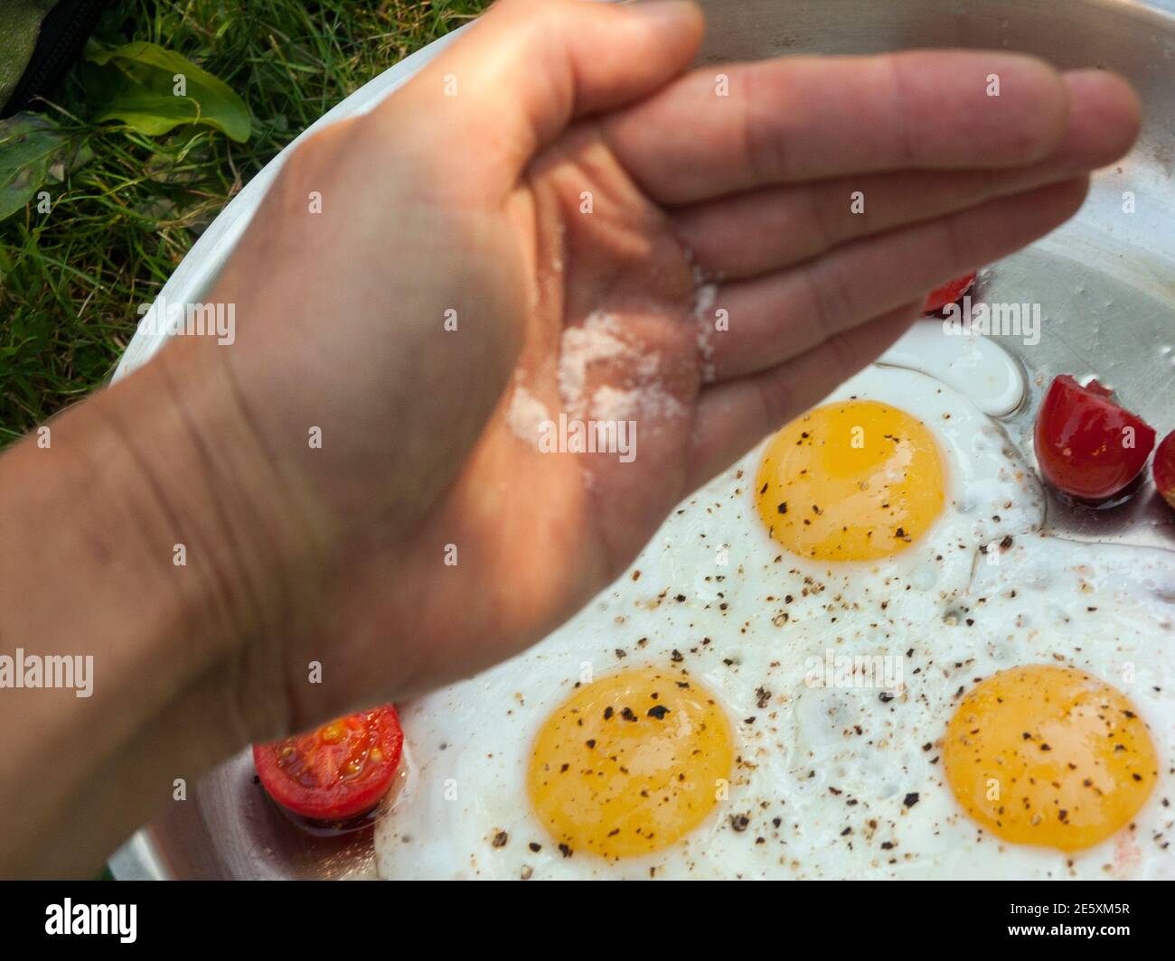 A hand adding salt in fried eggs, selective focus close-up Stock Photo