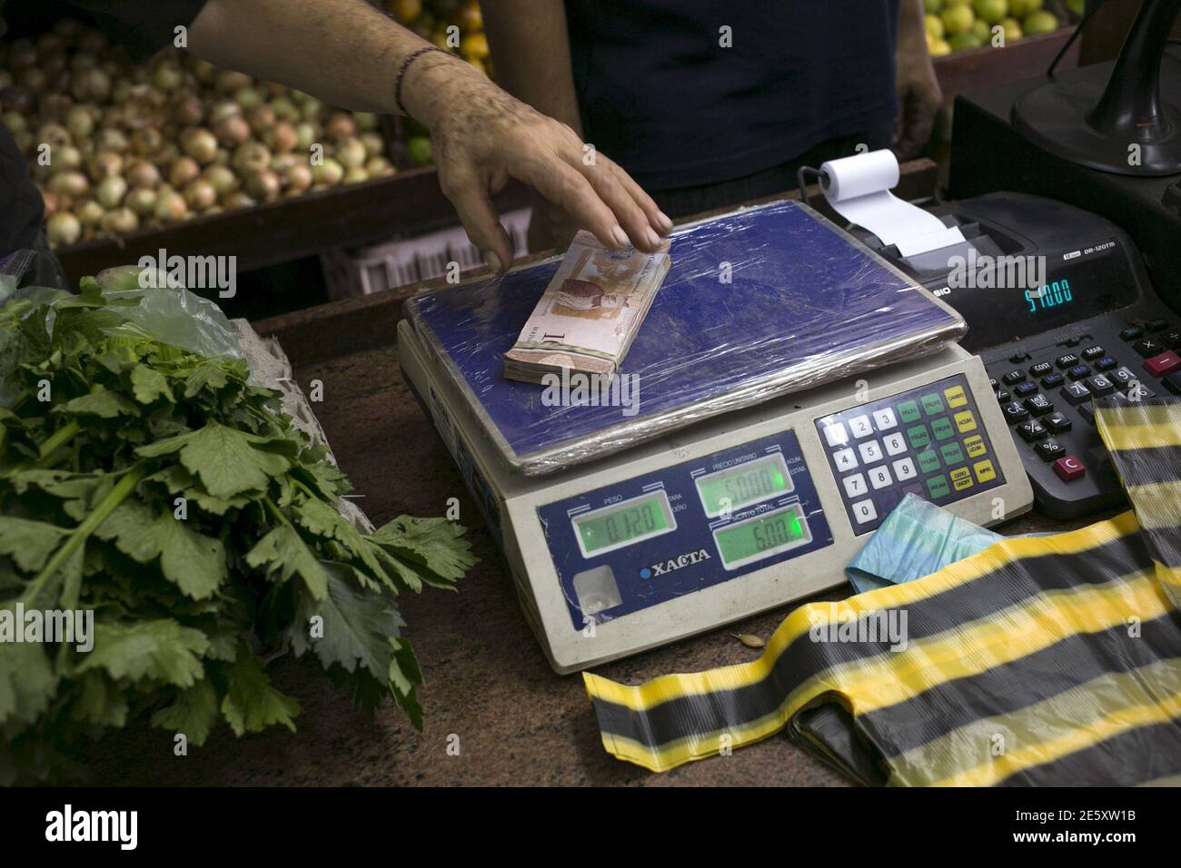 A clerk grabs a stack of Venezuelan 10 bolivars banknotes at a fruit and vegetable store in Caracas July 10, 2015. A debilitating recession and a drop in oil prices have harmed the OPEC nation's ability to provide dollars through its complex three-tiered currency control system, pushing up the black market rate at a dizzying speed. The bolivar sank past 600 per U.S. dollar on Thursday, compared with 73 a year ago, according to anti-government website DolarToday. REUTERS/Marco Bello Stock Photo