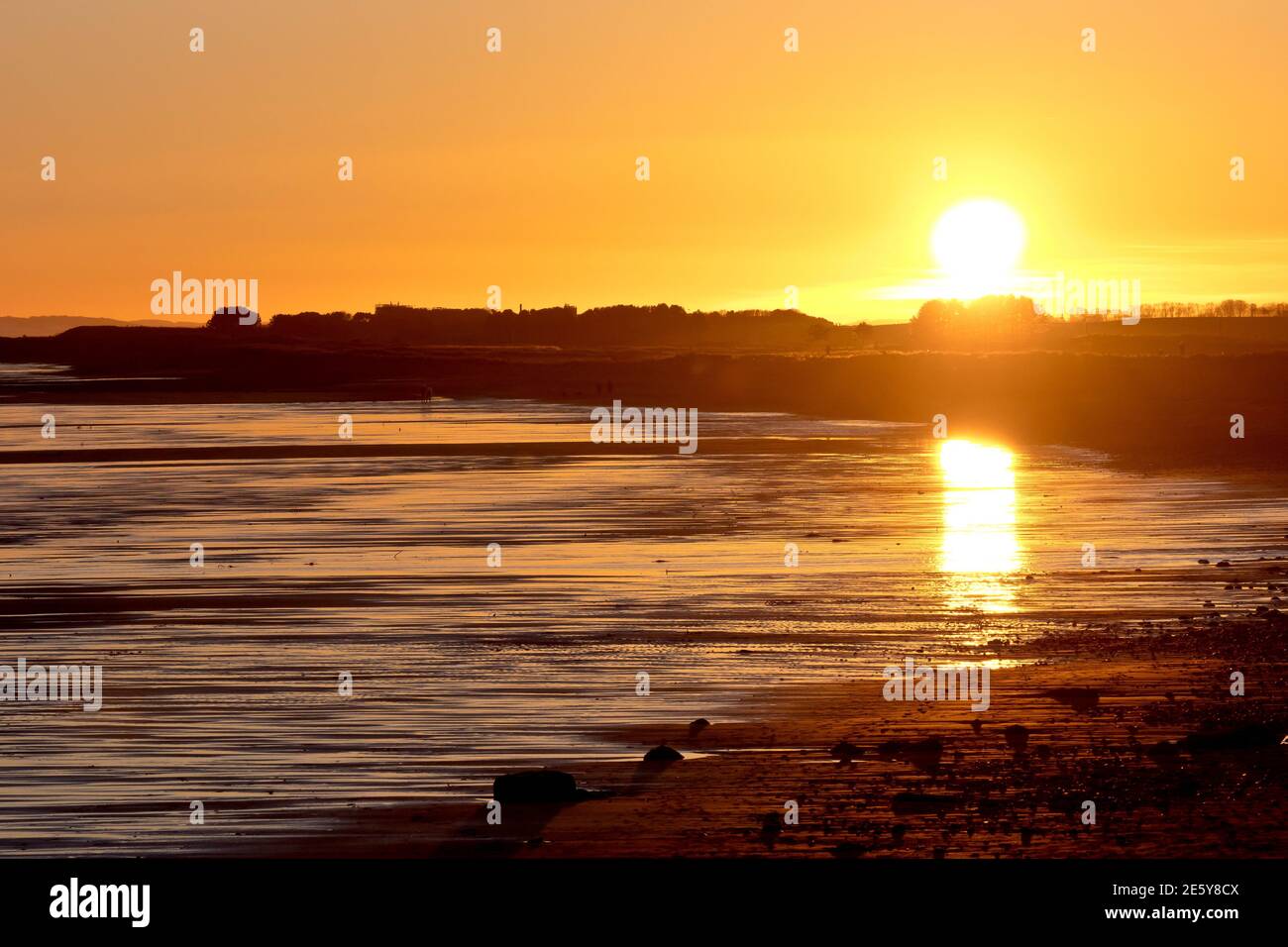 The sun begins to set over the beach at Arbroath at the end of a winters day, its light reflected in the wet sands. Stock Photo