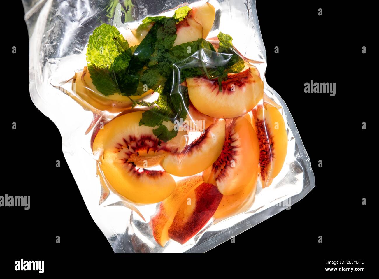 peach slices with mint leaves vacuum packed sealed for sous vide cooking.backlight on black background Stock Photo