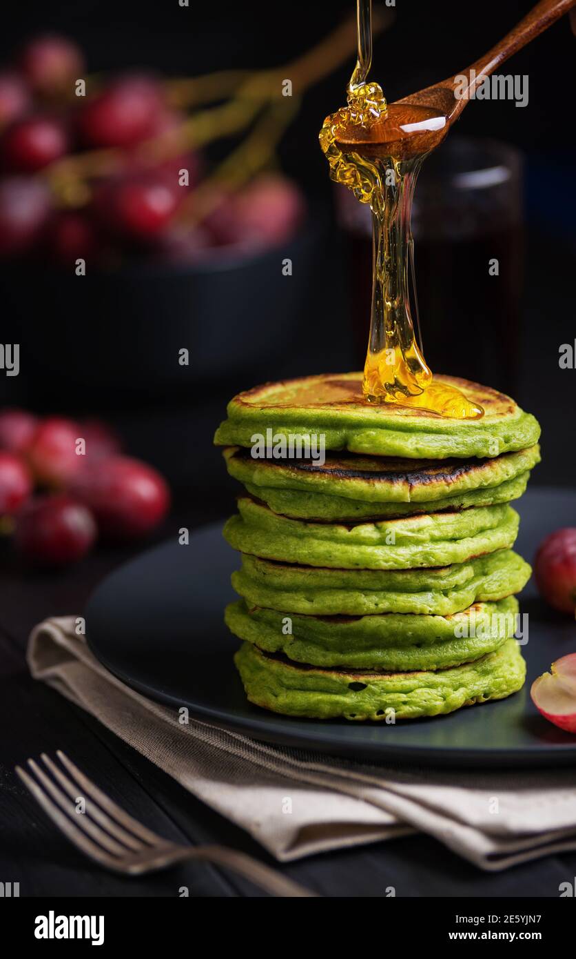 Green pancakes with matcha tea or spinach, dressed honey and red grapes. Ideas and recipes for healthy breakfast with superfood ingredients. Dark back Stock Photo