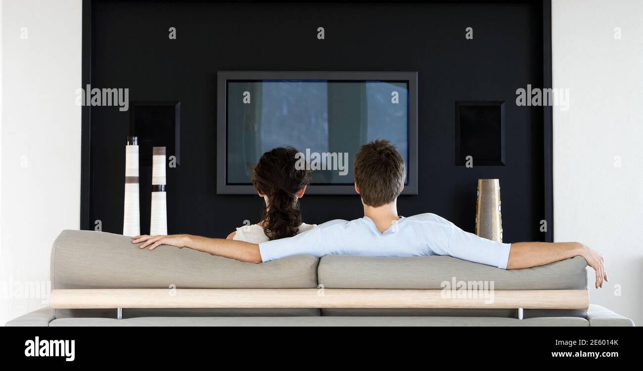 Rear view of young couple watching TV together in living room Stock Photo