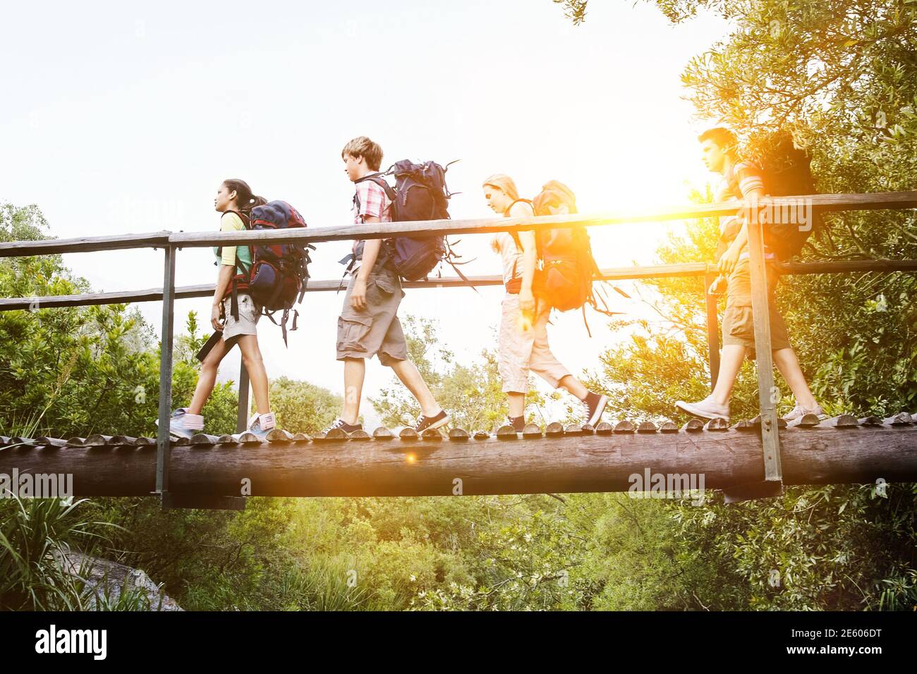 Teenage boys and girls with backpacks walking on bridge in forest Stock Photo