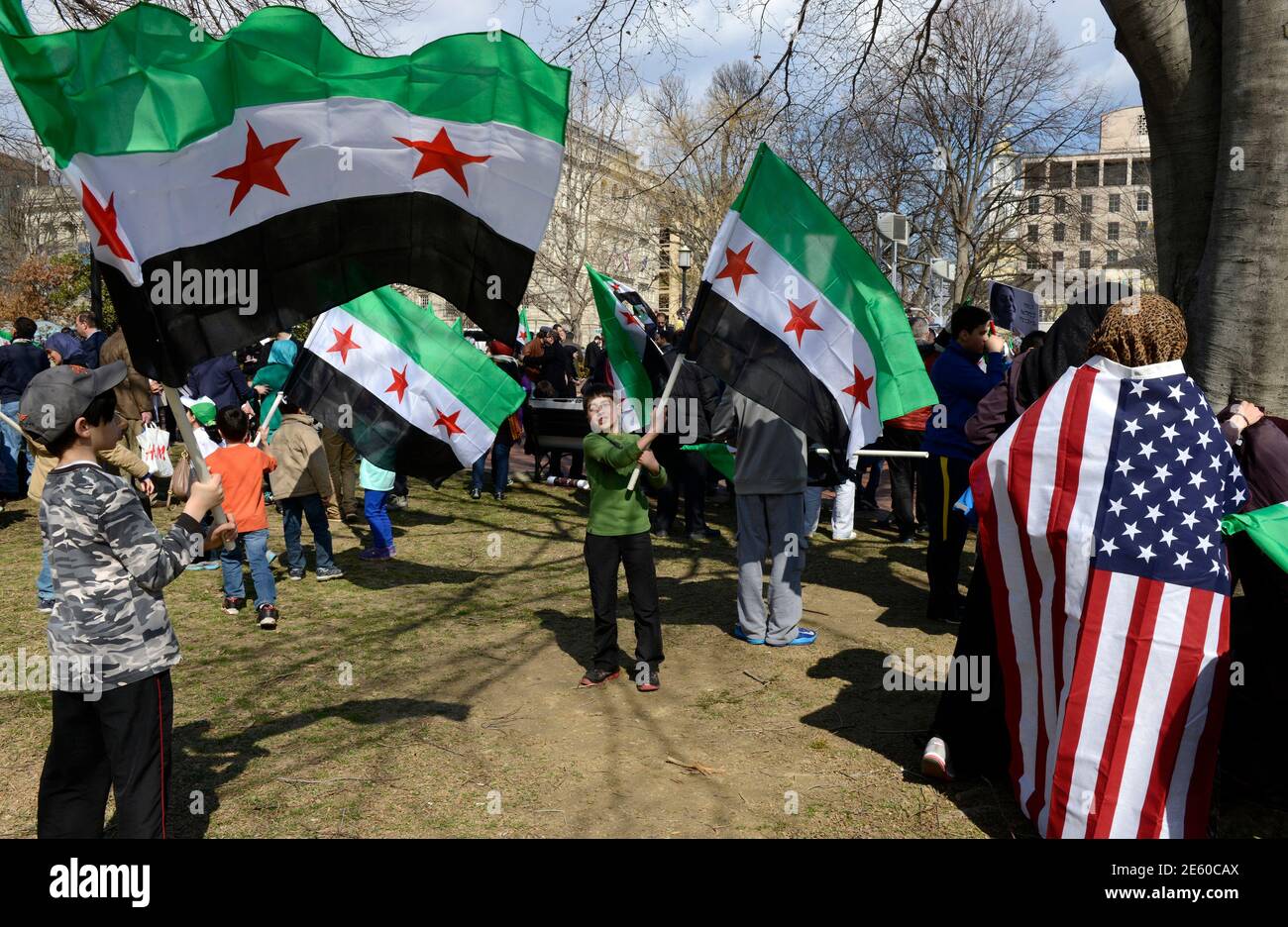 Nawal Abdul of Dearborn, Michigan (R) wears an American flag as her family waves Syrian flags (L) as they join dozens of protestors gathered to mark the 3rd anniversary of the Syrian revolution. in Lafayette Park, across from the White House, in Washington, March 15, 2014. The anti-Assad regime demonstrators called for an end to the violence, where reportedly more than 100,000 people have lost their lives, leaving cities and towns devastated and millions of refugees.         REUTERS/Mike Theiler   (UNITED STATES - Tags: POLITICS CIVIL UNREST) Stock Photo