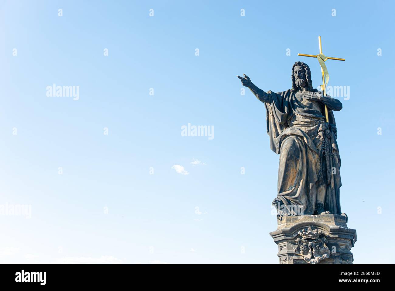 Ancient statue of a saint monk with a cross at the Charles Bridge in Prague at blue sky and copy space, Czech Republic, summer Stock Photo