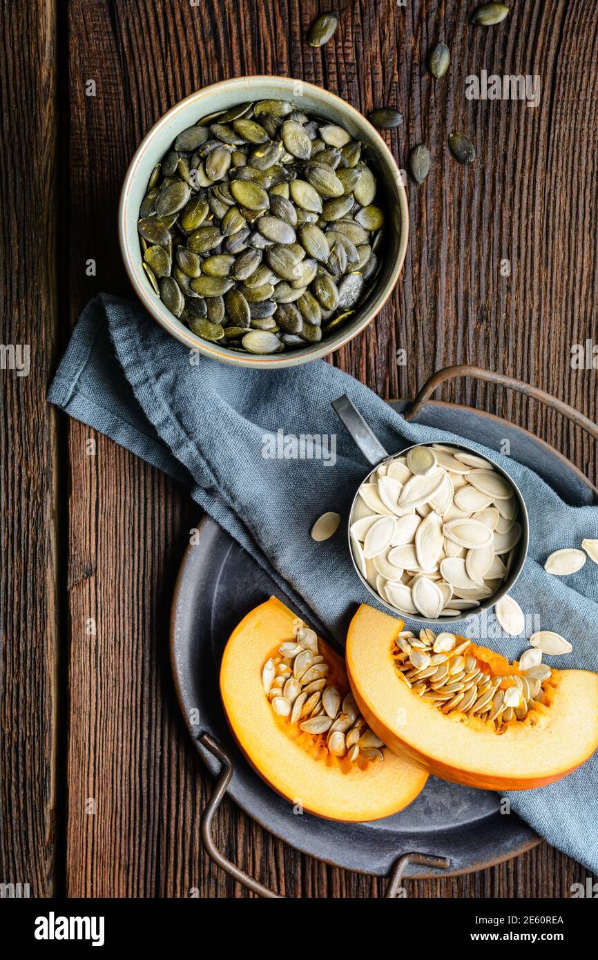 Pumpkin seeds in ceramic bowl, decorated with pumpkin slices on wooden table Stock Photo