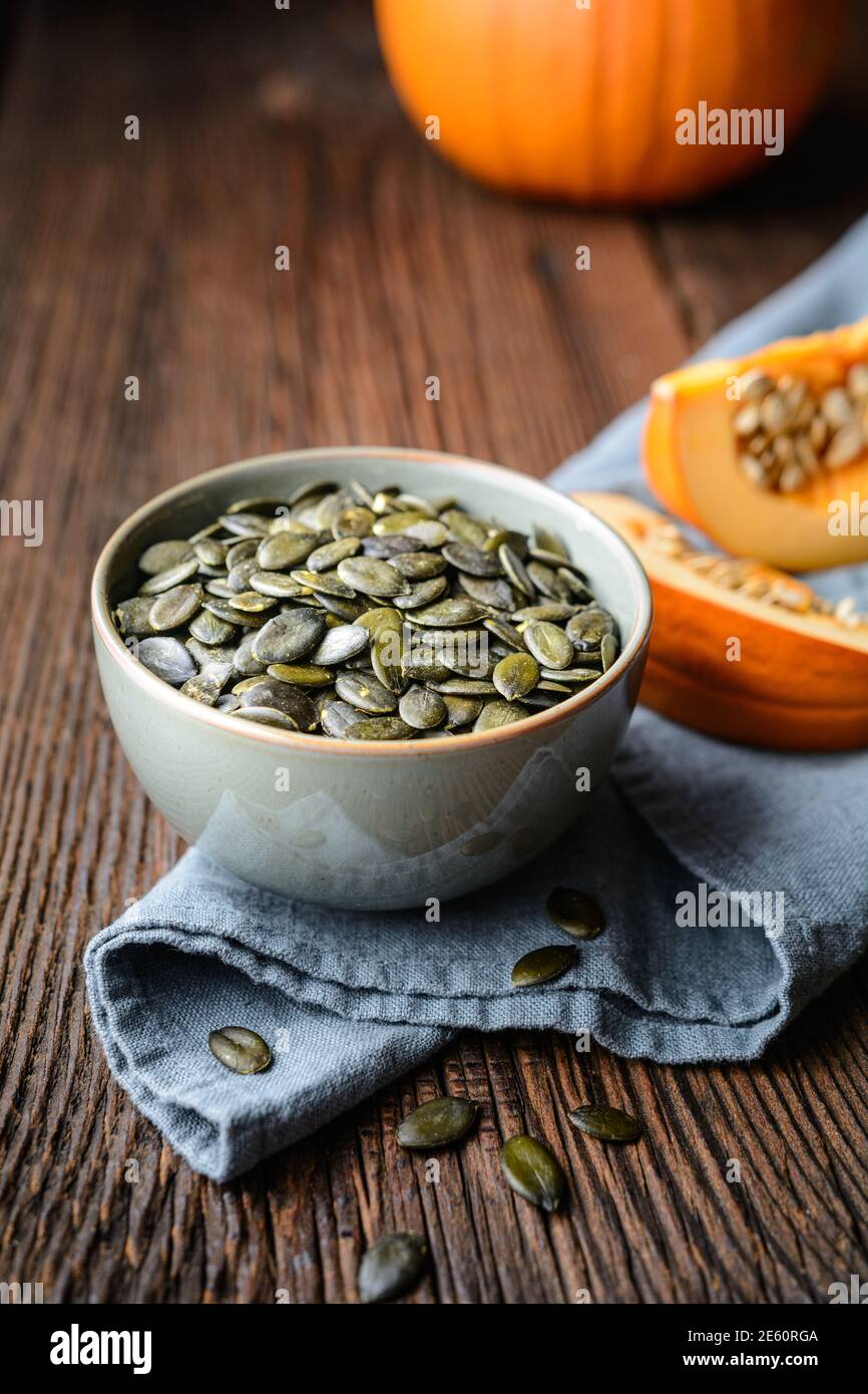 Pumpkin seeds in ceramic bowl, decorated with pumpkin slices on wooden table Stock Photo