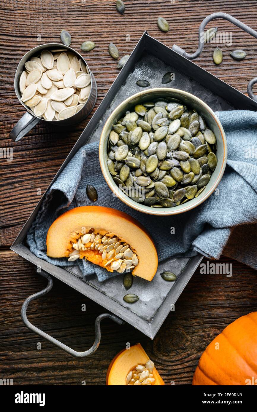 Pumpkin seeds in ceramic bowl, decorated with pumpkin slices on wooden table Stock Photo