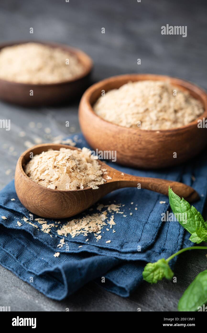 Dietary supplement, unfortified nutritional yeast flakes in a wooden bowl and scoop on stone backdrop Stock Photo