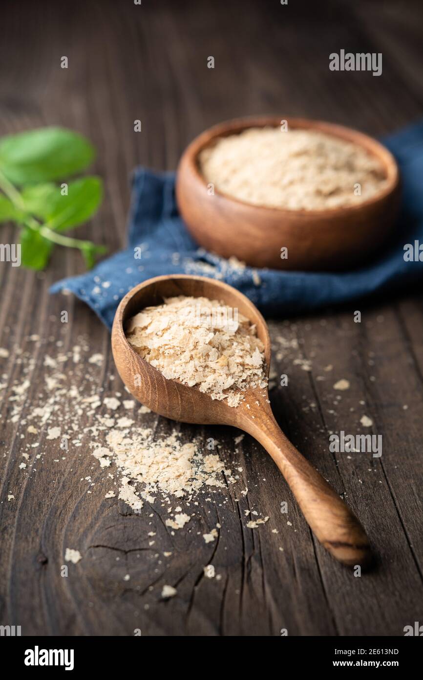 Dietary supplement, unfortified nutritional yeast flakes in a wooden bowl and scoop on wooden table Stock Photo