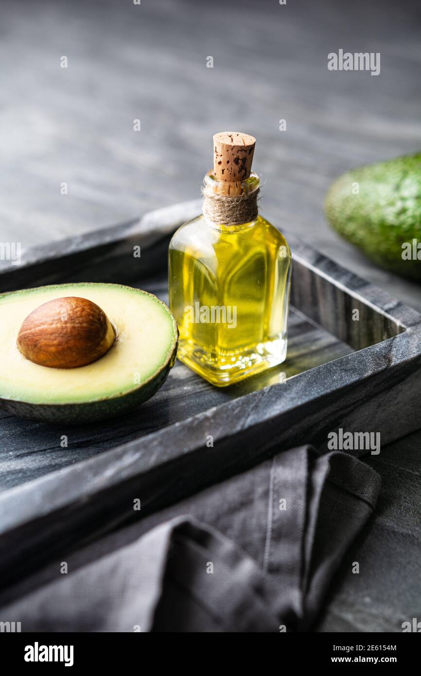 Healthy avocado oil in a glass bottle, decorated with sliced avocado on stone background Stock Photo