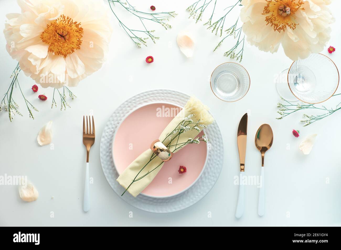 Effortless golden birthday dinner table decor. Pale yellow peony flowers. White dinner table, white and gold utensils, decorated with season flowers Stock Photo