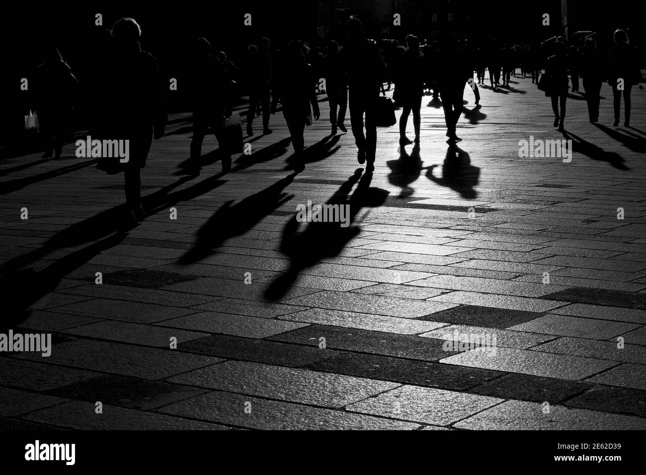 Shadows of people walking at sunset on the stone floor of the pre-pandemic city of Milan, Lombardy, Italy Stock Photo