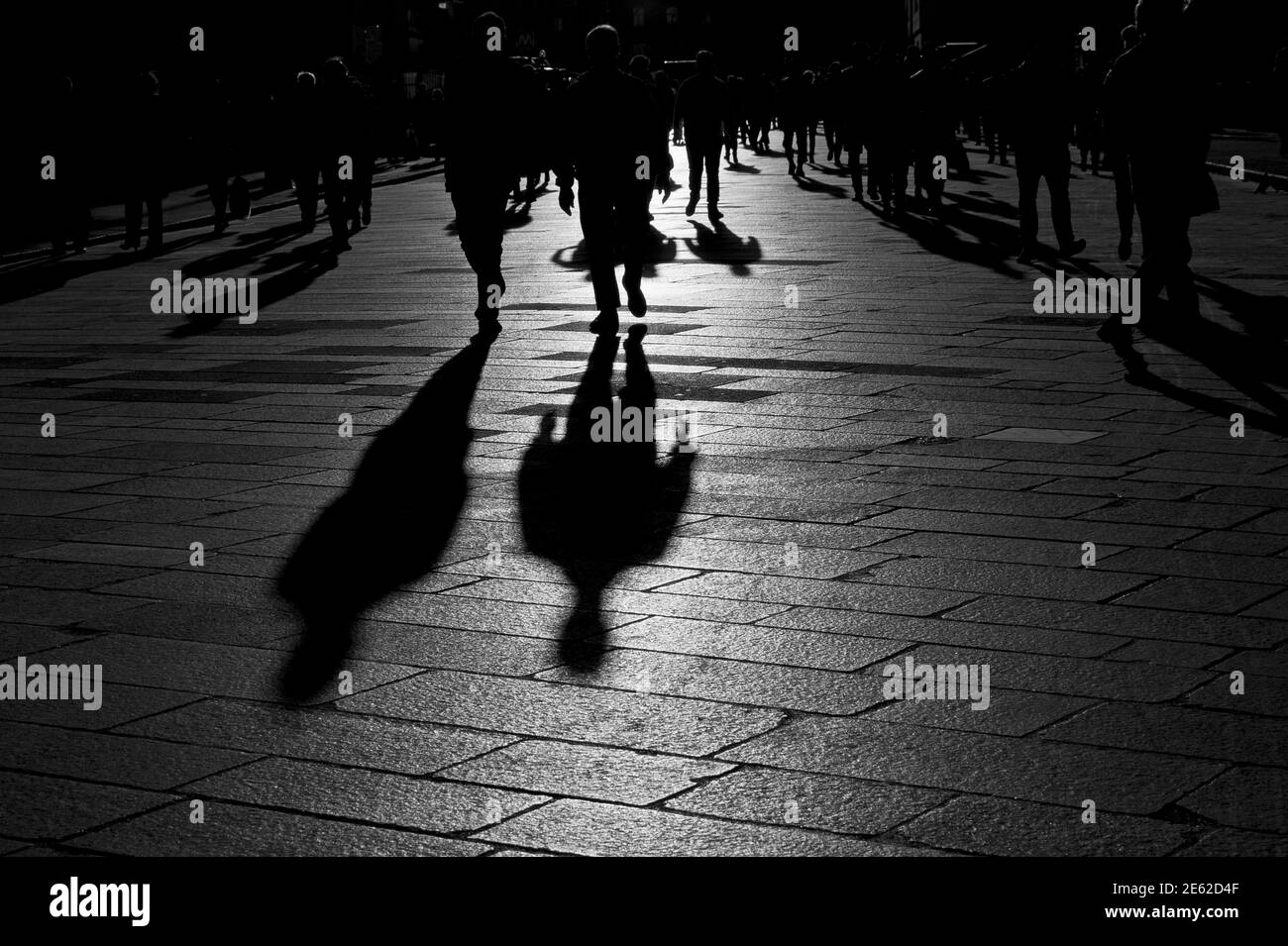 Shadows of people walking at sunset on the stone floor of the pre-pandemic city of Milan, Lombardy, Italy Stock Photo