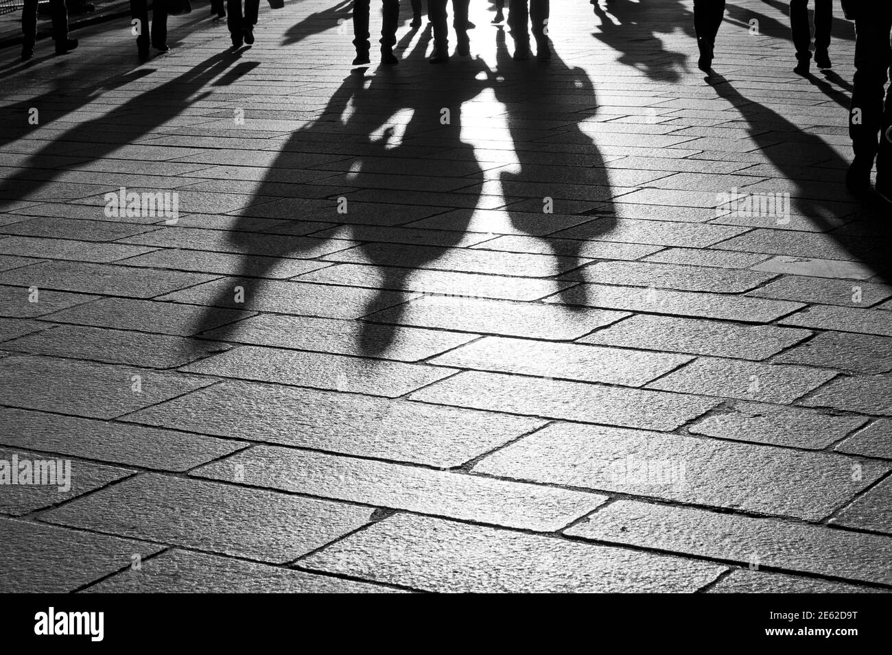 Shadows of people walking at sunset on the stone floor of the pre-pandemic city of Milan, Lombardy, Italy Stock Photo