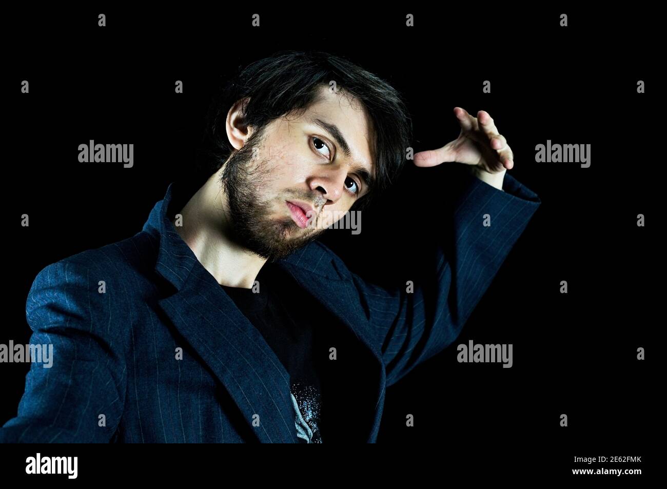 Young man looking down with his left hand up doing a pose, head tilted Stock Photo