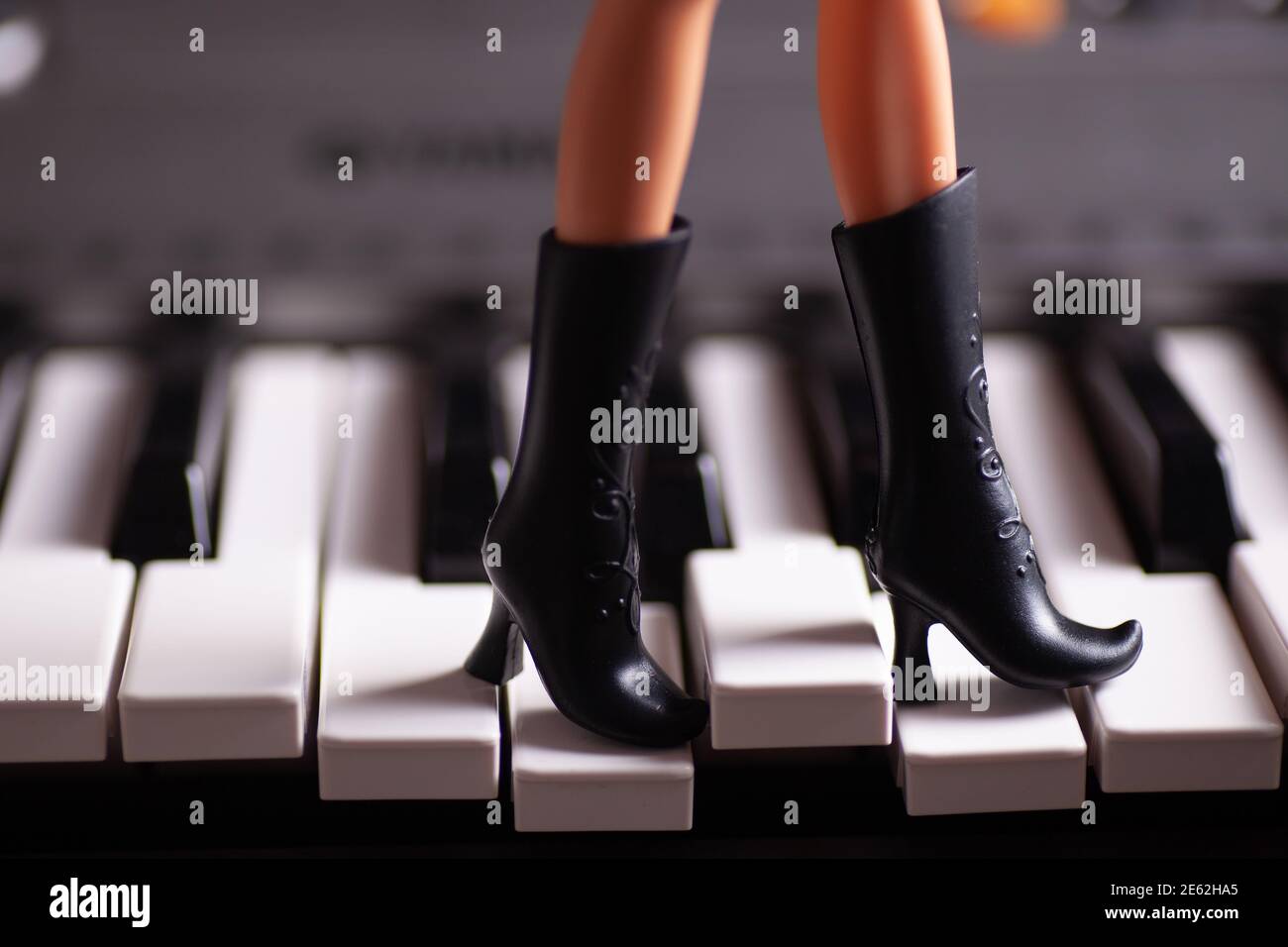 Close-up slim plastic legs in black toy rubber boots with high heels step on piano keys Stock Photo