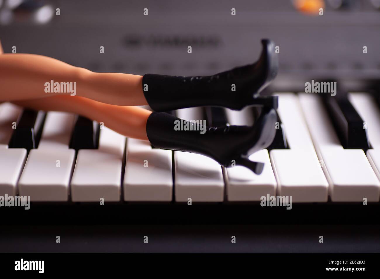 Close-up slim plastic legs in black toy rubber boots with high heels lie on piano keys Stock Photo