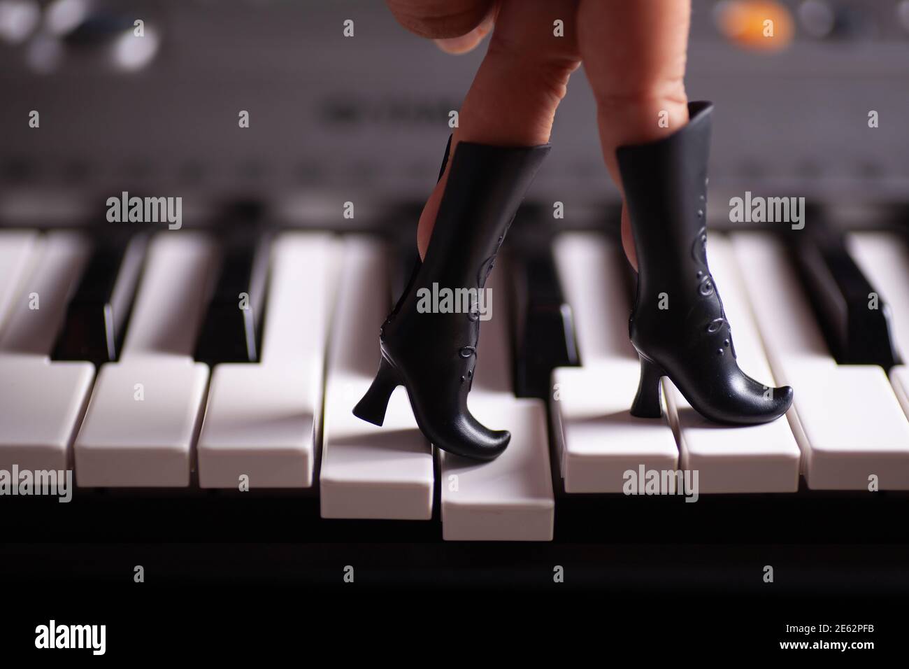 A close-up hand with fingers stuck in a toy black doll's boots steps on the piano keys Stock Photo