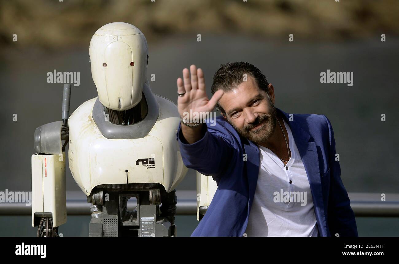 Spanish actor Antonio Banderas waves alongside a robot used in the film  Automata during a photocall on the third day of the 62nd San Sebastian Film  Festival, September 21, 2014. Banderas stars