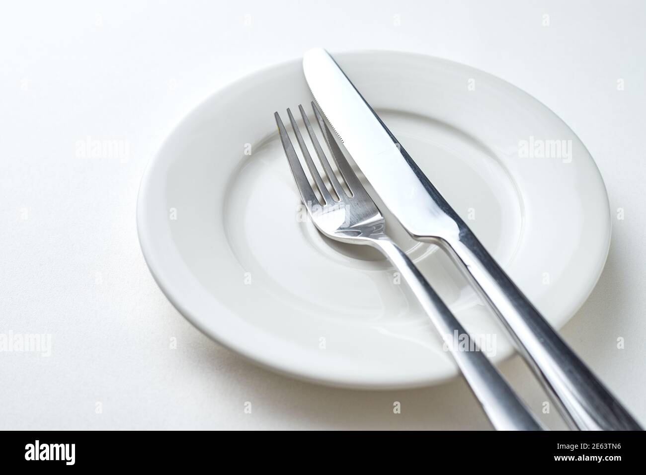Fork and knife on a white plate on a white background Stock Photo - Alamy