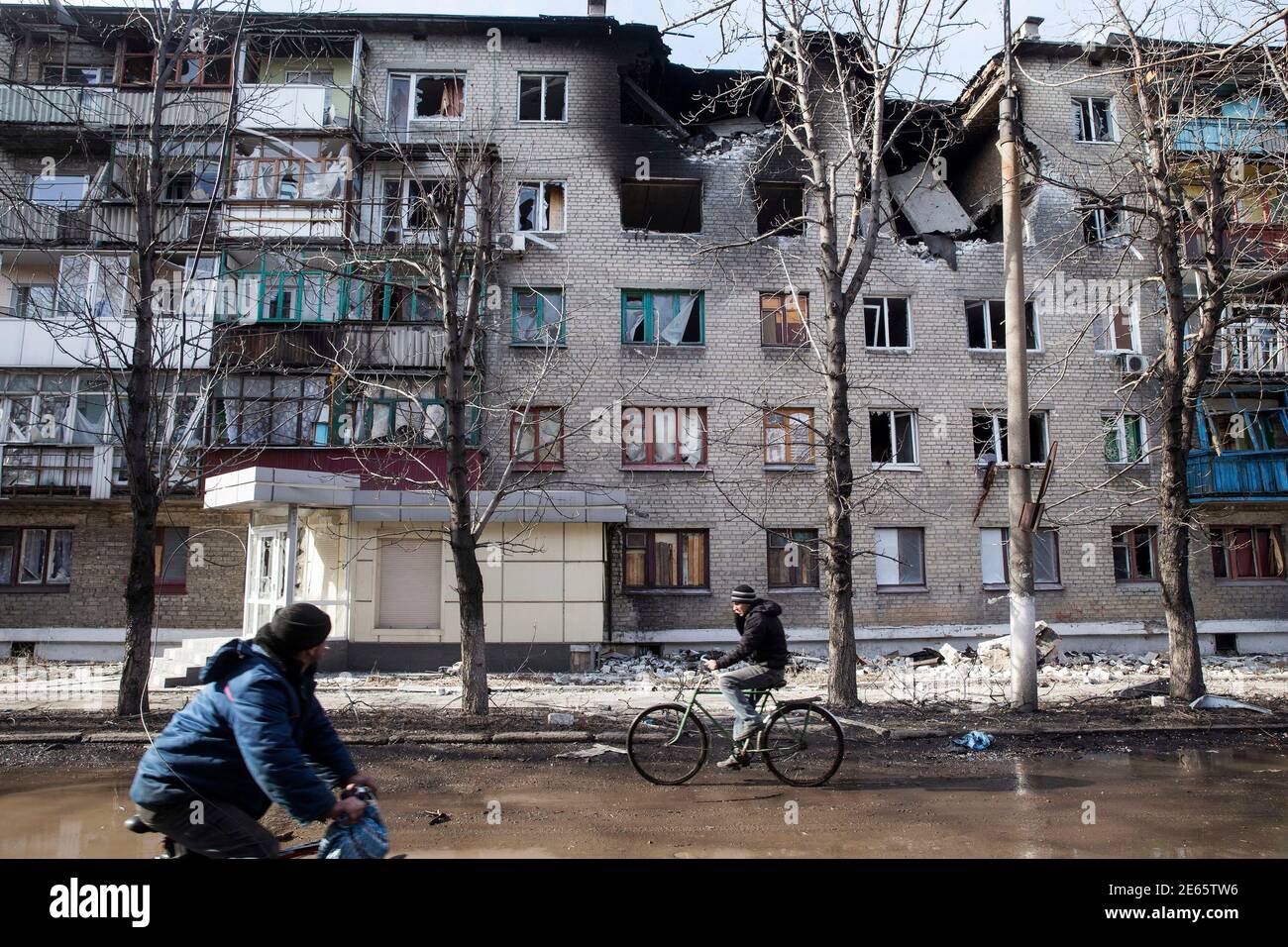 Men ride bicycles past a building which was damaged by fighting in the town of Debaltseve February 23, 2015. Fighting over the railway hub of Debaltseve intensified in the days following a ceasefire deal meant to have taken effect on Feb. 15. Rebels who had encircled the town launched a massive assault, routing all Ukrainian forces by Feb. 18. The battle for the town caught civilians in the crossfire on a scale not yet seen in the war that has killed nearly 6,000 people. Most residential buildings in the town have been damaged by shelling or are burnt out. Picture taken February 23, 2015. REUT Stock Photo