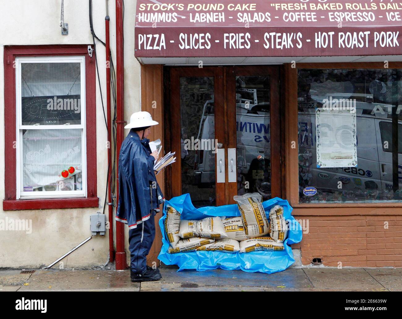 A postal worker walks past a sandbagged restaurant as he delivers mail in wind and rain from Hurricane Sandy on Main street in the Manayunk section of Philadelphia, Pennsylvania, October 29, 2012. Hurricane Sandy, the monster storm bearing down on the U.S. East Coast, strengthened on Monday after hundreds of thousands moved to higher ground, public transport shut down and the U.S. stock market suffered its first weather-related closure in 27 years.  REUTERS/Tim Shaffer (UNITED STATES - Tags: ENVIRONMENT) Stock Photo