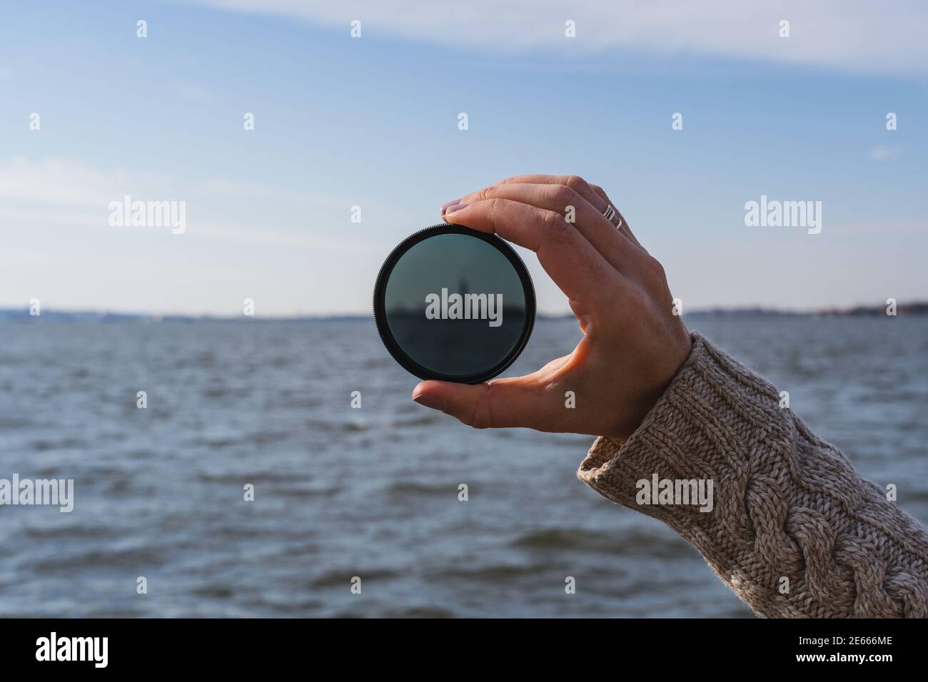 A photo of a hand holding up a lens filter, with the Statue of Liberty