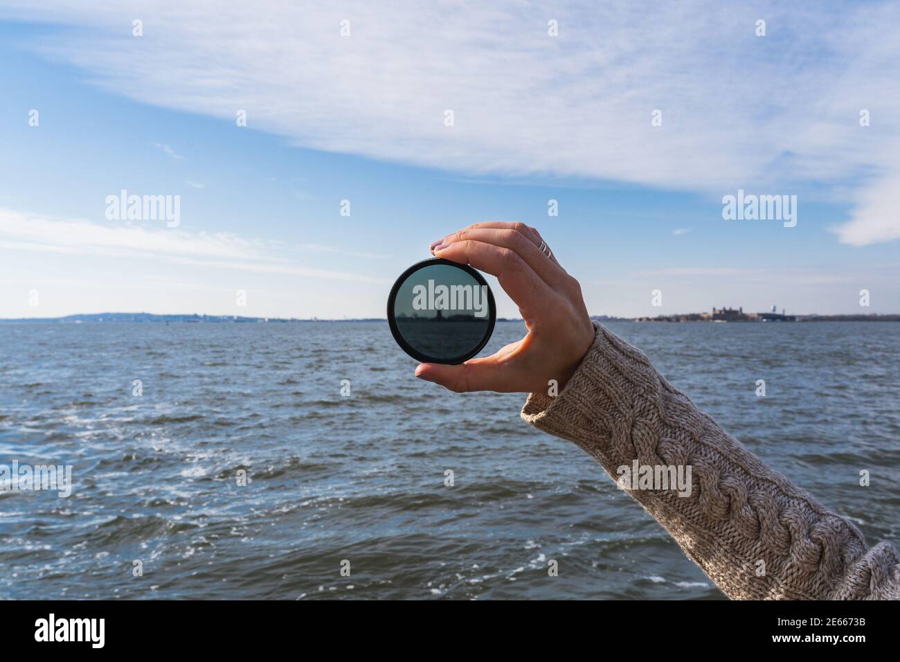 A photo of a hand holding up a lens filter, with the Statue of Liberty