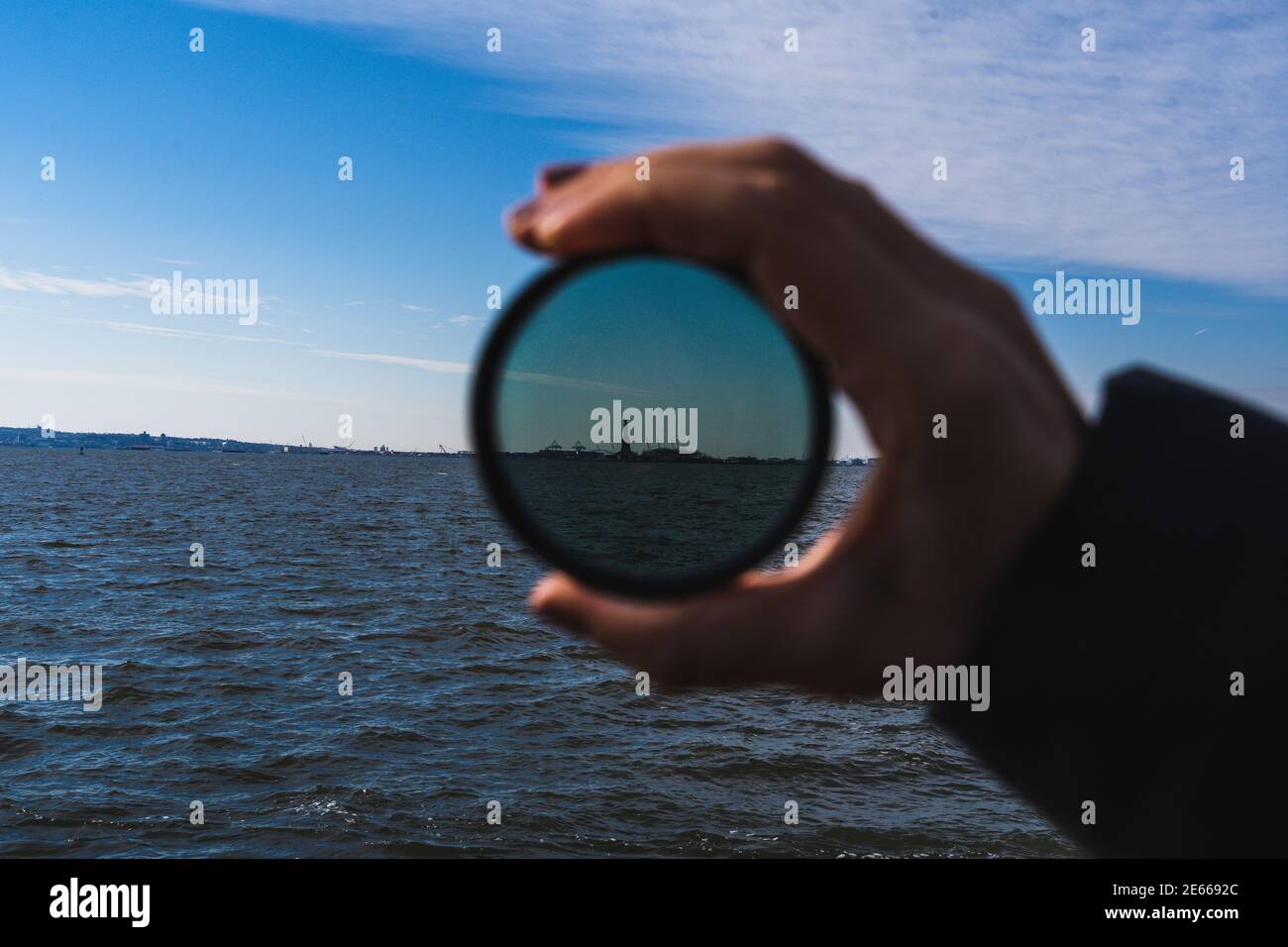 A photo of a hand holding up a lens filter, with the Statue of Liberty