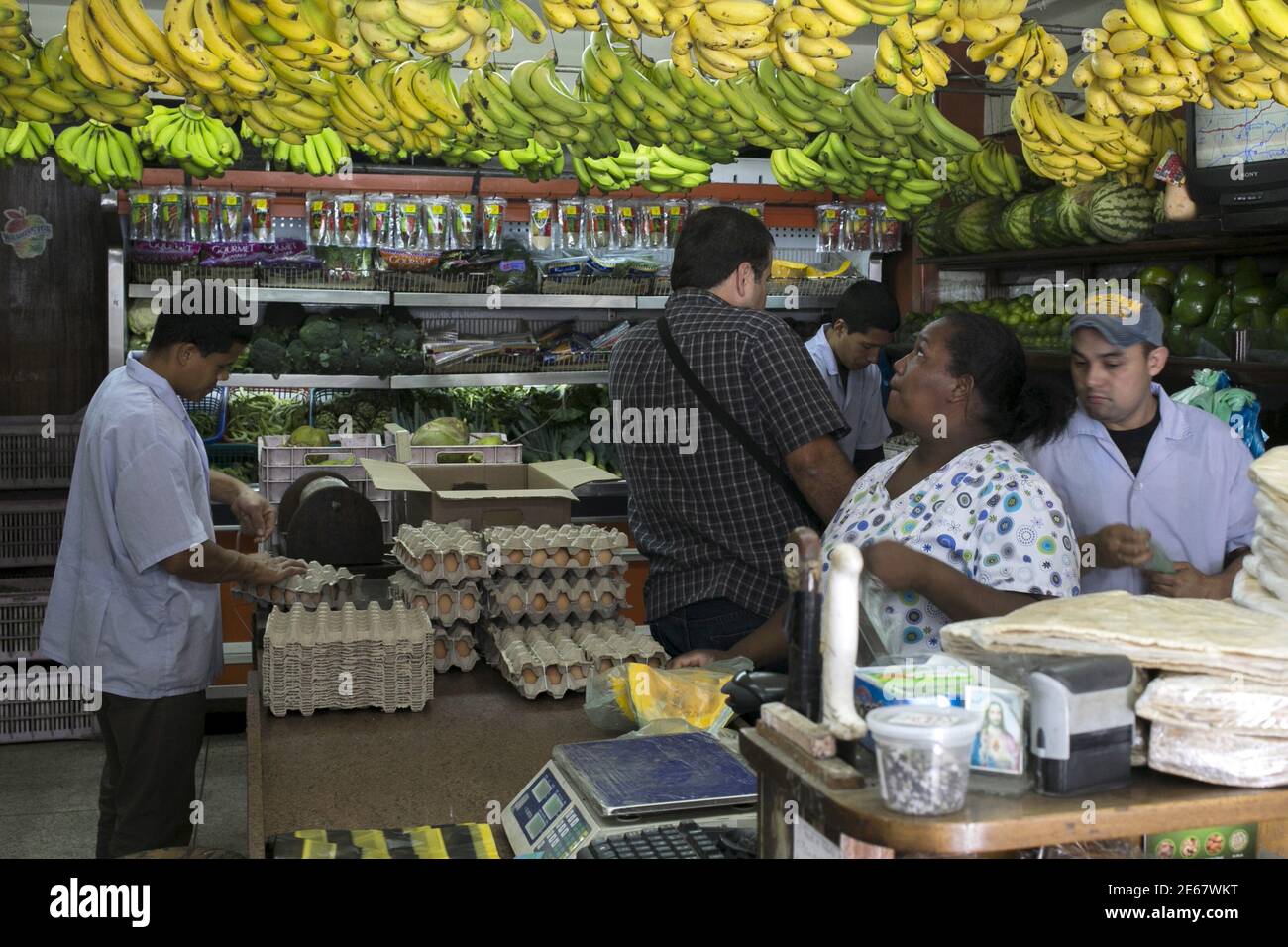 A customer selects bananas as others buy goods at a fruit and vegetable store in Caracas, July 10, 2015. A debilitating recession and a drop in oil prices have harmed the OPEC nation's ability to provide dollars through its complex three-tiered currency control system, pushing up the black market rate at a dizzying speed. The bolivar sank past 600 per U.S. dollar on Thursday, compared with 73 a year ago, according to anti-government website DolarToday.REUTERS/Marco Bello Stock Photo