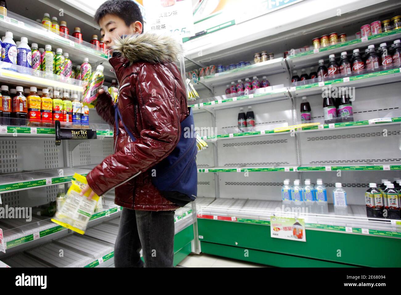 A customer stands near shelves of bottled drinks that are running out at a convenience store in central Tokyo March 24, 2011. Many shops in Tokyo ran out of bottled water on Thursday after radiation from a damaged nuclear plant made tap water unsafe for babies, while more countries imposed curbs on imports of Japanese food. Engineers are trying to stabilise the Fukushima nuclear facility nearly two weeks after an earthquake and tsunami battered the complex and devastated northeast Japan.   REUTERS/Aly Song (JAPAN - Tags: DISASTER FOOD SOCIETY) Stock Photo
